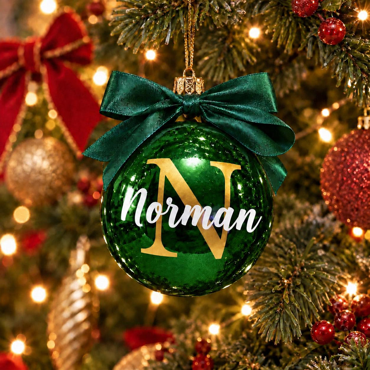 Green personalised Christmas bauble with gold initial N and the name Norman, finished with a matching green ribbon, hanging on a Christmas tree