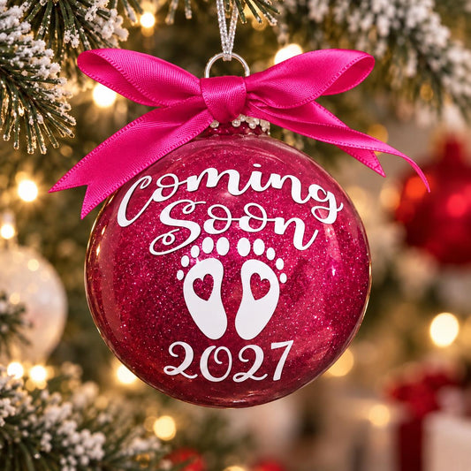Pink Coming Soon 2027 pregnancy announcement Christmas bauble with baby footprints and matching ribbon on a tree