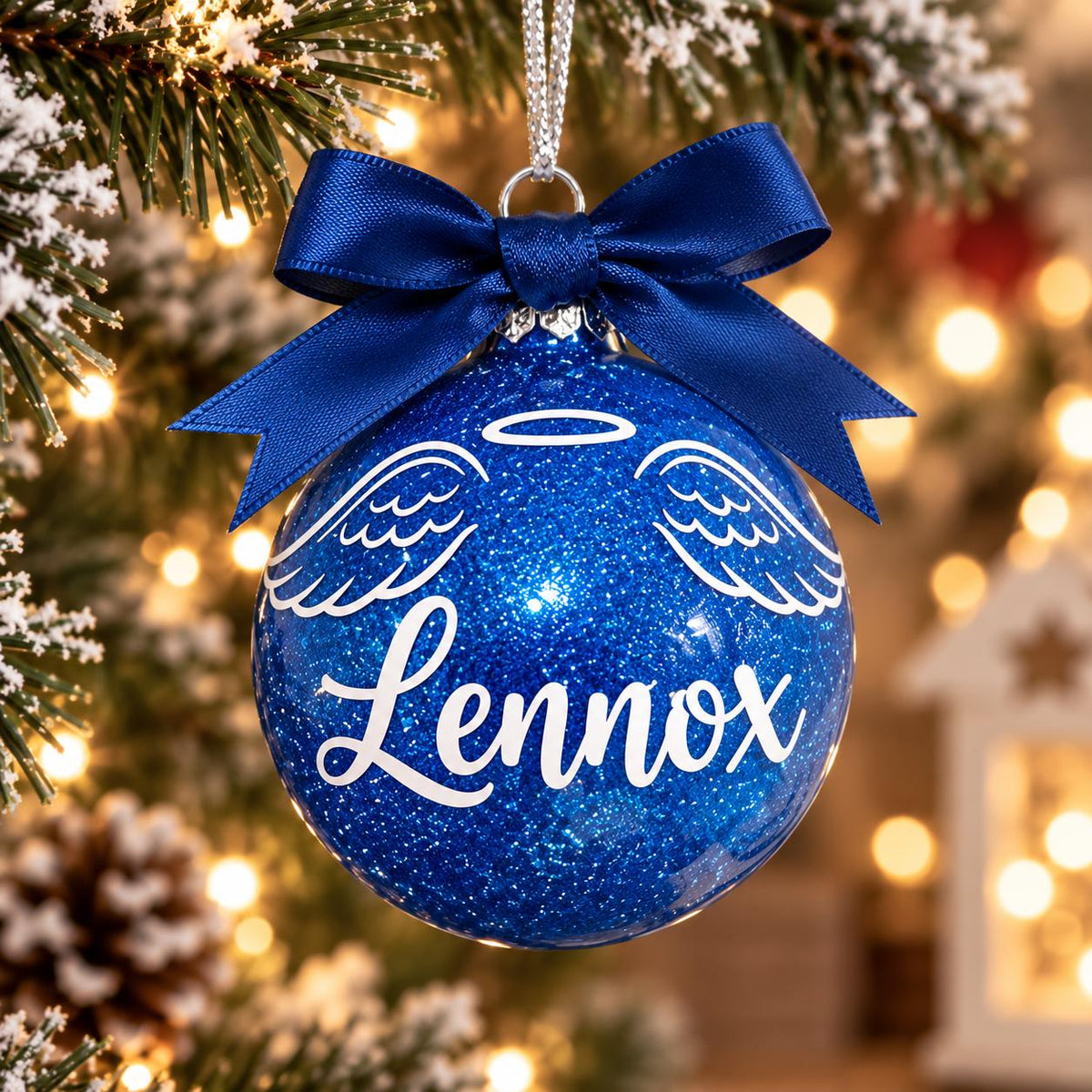 Blue personalised memorial Christmas bauble with angel wings, halo, name Lennox and matching ribbon on a tree